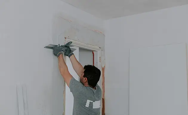 Technician patching a rectangular hole in interior drywall with putty knife